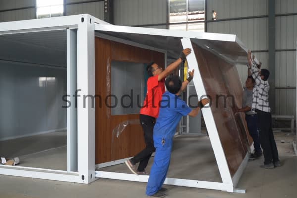 Workers installing wall panel on modular house