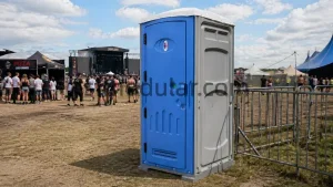 Portable toilet for events placed at an outdoor music festival with stage, crowd barriers, tents, and temporary public sanitation area
