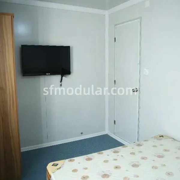 prefabricated-shelter-bedroom-interior-tv-door Interior room of a prefabricated shelter with bed, door and wall mounted TV