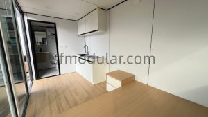 Interior view of an apple cabin featuring a compact kitchenette and wooden flooring