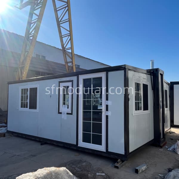 small-expandable-homes-prefab-structure-with-windows A semi-assembled small expandable home with white window frames and glass entry doors in a manufacturing warehouse